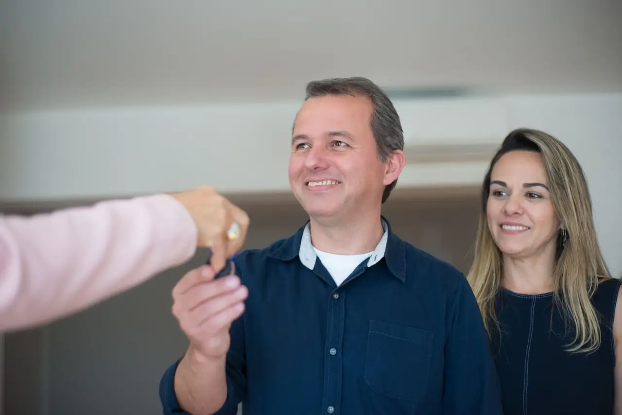 Smiling couple receiving keys, celebrating new home purchase indoors.