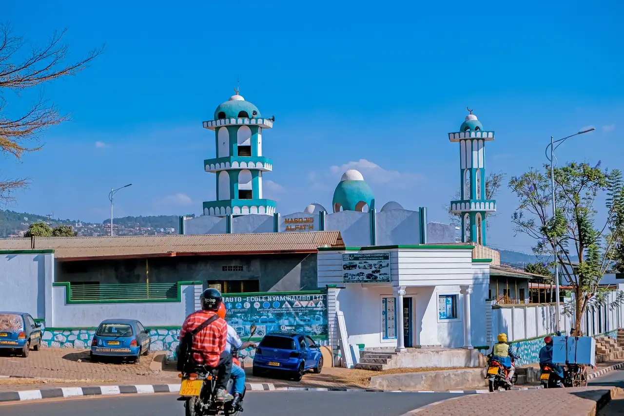 Vibrant urban street with a mosque, motorcycles, and parked cars on a sunny day.