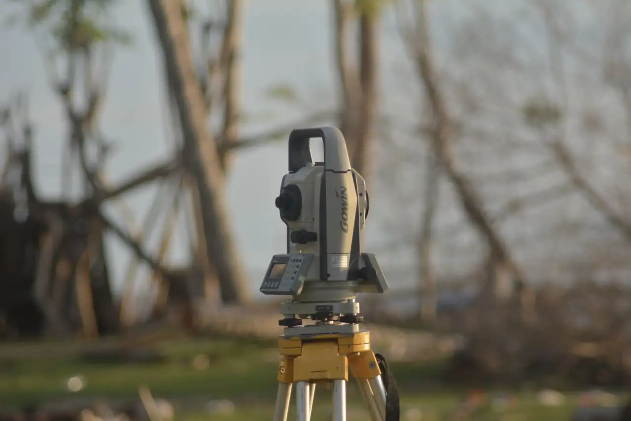A precise total station used for geodetic surveying at a construction site with a natural background.