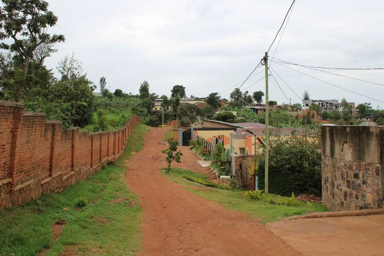 Scenic view of a dirt road in Kigali with red brick walls and lush greenery.
